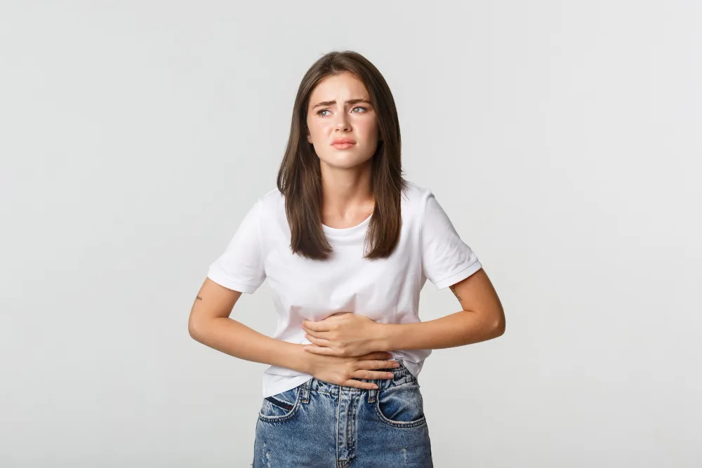 Young woman experiencing Menstrual Pain while holding her lower abdomen with both hands, illustrating discomfort associated with period cramps.