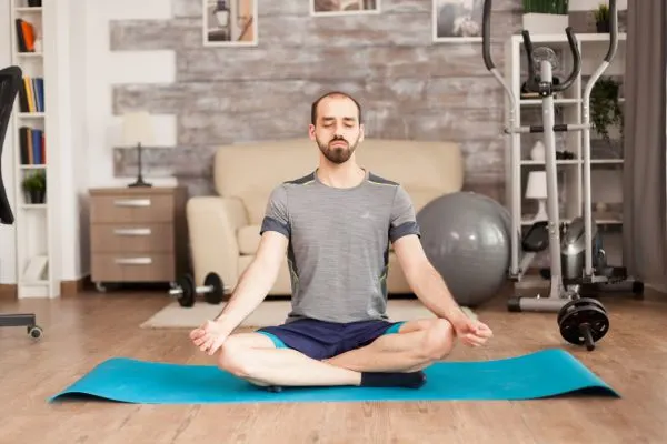 Man practicing seated meditation with deep breathing on a yoga mat to promote relaxation and reduce daily stress.