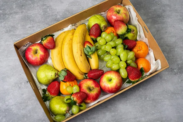 Fresh fruit box filled with bananas, apples, grapes, and strawberries, perfect for healthy eating fruit at night.