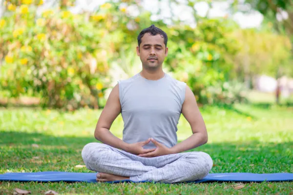 Man practicing serene cross-legged meditation outdoors on a blue mat, focusing on Yoga and Longevity wellness.