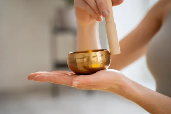 Sound Healing Reduce Workplace Stress session featuring a woman holding a small Tibetan singing bowl with wooden mallet